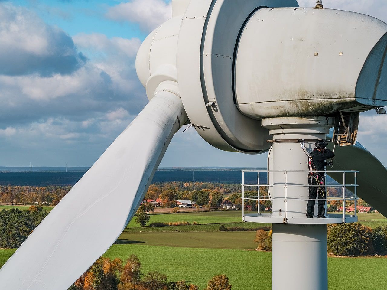 Ein Mann steht auf der Spitze einer Windturbine und blickt in die Ferne, umgeben von einem klaren blauen Himmel.