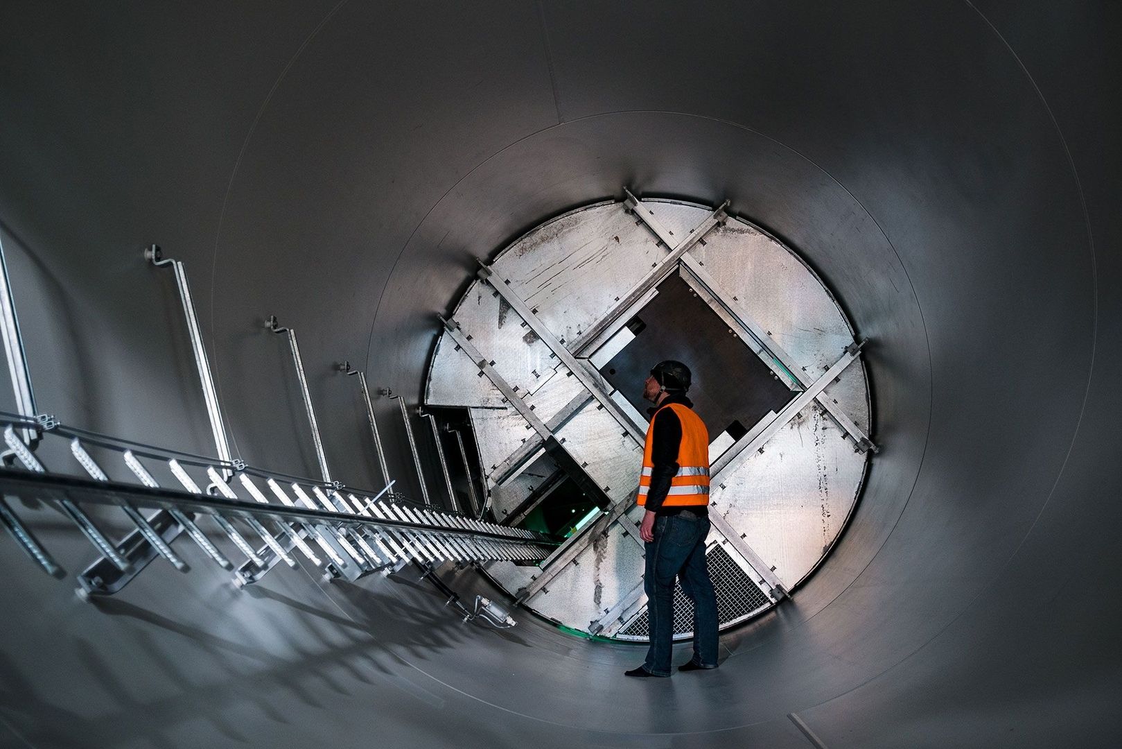 Ein Mann steht in einem großen Metallrohr und blickt nach vorne, umgeben von der glatten, reflektierenden Oberfläche.