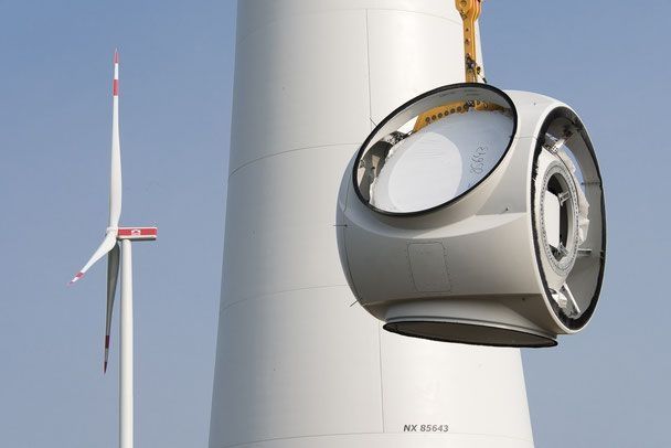 A crane lifts a large wind turbine to install it at its site.