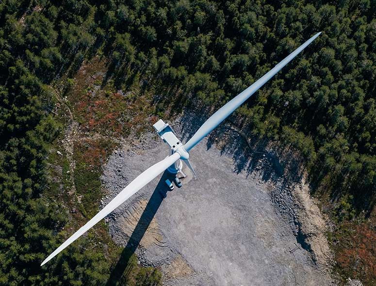 Luftaufnahme einer Windkraftanlage, umgeben von dichtem Wald, der die nachhaltige Energieerzeugung symbolisiert.